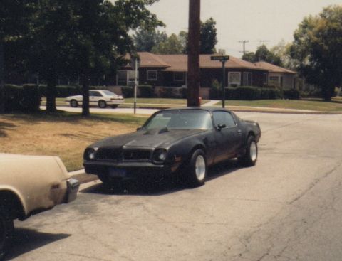 1968 Ford Mustang - A black coupe with white wheels is parked on a residential street next to another car.