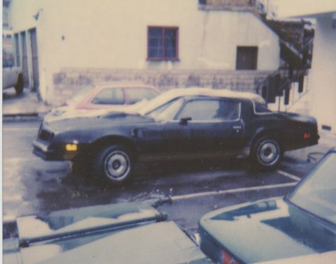 1968 Ford Mustang - A dark-colored Pontiac Firebird is parked in a lot, partially covered in snow.