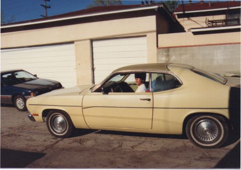 1968 Ford Mustang - A beige 1973 Plymouth Duster is parked next to another vehicle, with a driver visible inside.