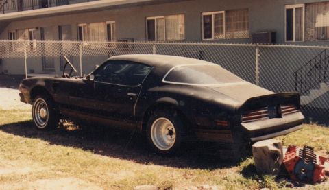 1968 Ford Mustang - A black coupe with its hood open sits in a grassy yard next to a chain-link fence.