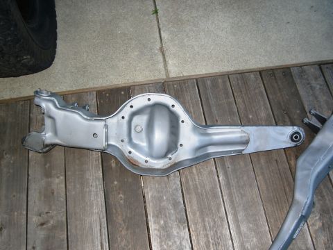 1986 Ford Bronco - A differential axle housing is shown on a wooden deck, with a tire visible in the upper left corner.