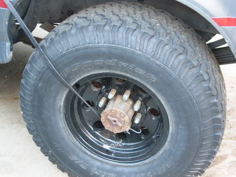 1986 Ford Bronco - A close-up view of a vehicle's tire and wheel assembly, showing off-road tire tread and a locking hub.