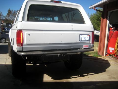 1996 Ford Bronco - The rear of a white Ford Bronco is shown parked in a driveway next to a garage with a red air compressor.