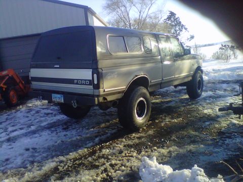 1994 Ford F-150 - A Ford pickup truck with a camper shell is parked in a snowy area next to a building.