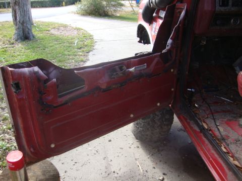 1986 Ford Bronco - The interior of a red vehicle is visible with the driver's door open, revealing worn and damaged interior components.