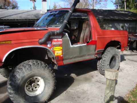 1986 Ford Bronco - This modified red SUV, likely a Ford Bronco from the early 1980s, features custom half doors and a snorkel intake.