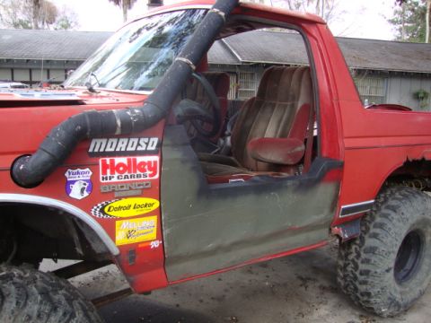 1986 Ford Bronco - A red Ford Bronco modified for off-roading, a snorkel and racing decals on the fender.