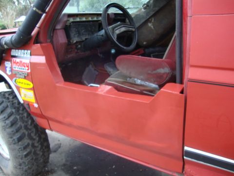 1986 Ford Bronco - The interior of a red off-road vehicle shows custom door cutouts and aftermarket parts, with visible stickers on the exterior fender.
