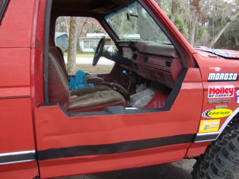 1986 Ford Bronco - This 1986 Ford Bronco features a custom half-door conversion and various racing decals on its exterior, hinting at its performance-oriented…