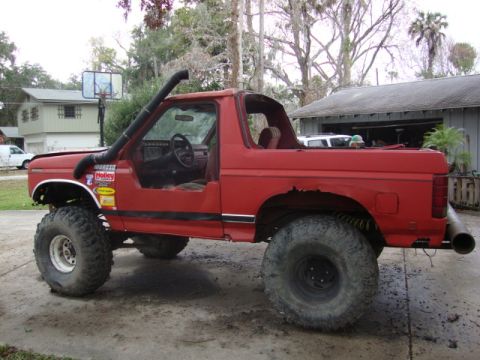 1986 Ford Bronco - This modified red SUV, likely from the 1980s, has been heavily altered for off-road use.