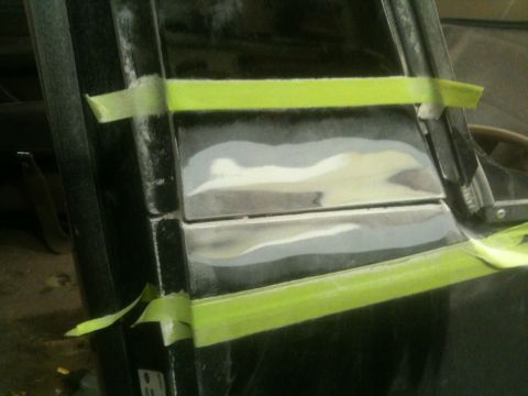 1993 Ford Bronco - Body filler and masking tape are applied to a vehicle's tailgate during a repair process.
