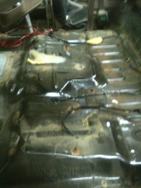 1993 Ford Bronco - The interior floor of a vehicle shows rust and exposed wiring, with a piece of yellow insulation.