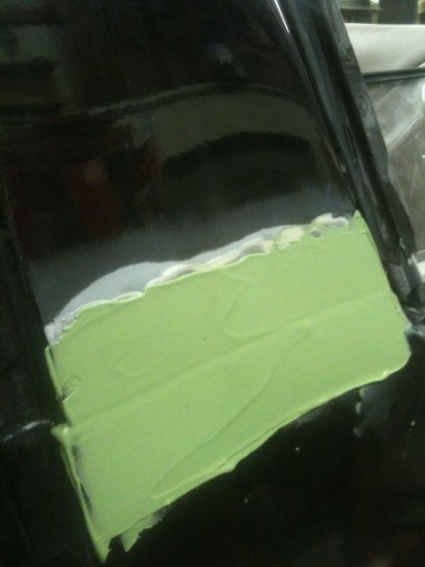 1993 Ford Bronco - Body filler is being applied to a black car panel, likely for repair work.