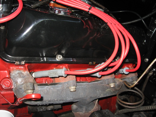 Close-up of red spark plug wires connected to spark plugs on an engine exhaust manifold
