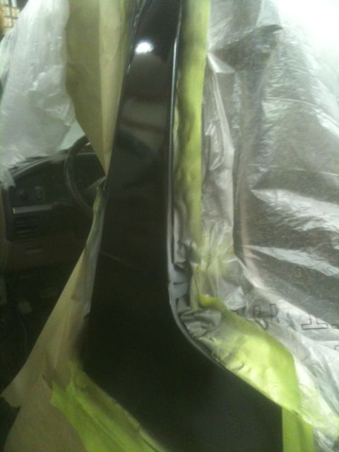 1993 Ford Bronco - A black painted car panel is covered in masking tape and plastic sheeting, possibly during a repair or painting process.
