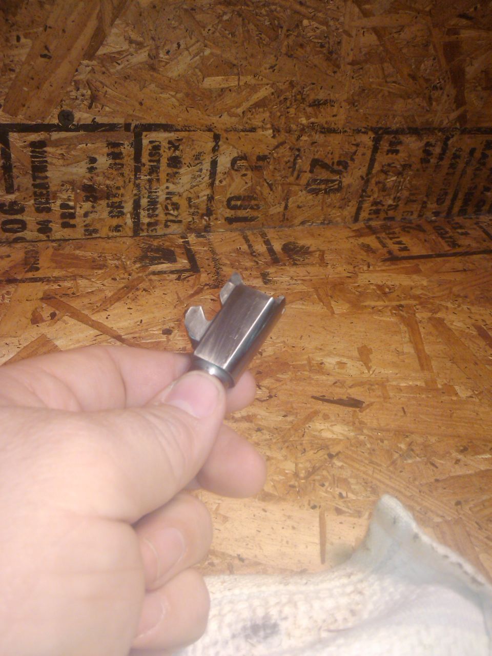 Metal part held in hand against a wood-paneled background