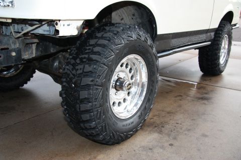1987 Ford Bronco - Close-up of a large off-road tire and wheel on a white SUV.