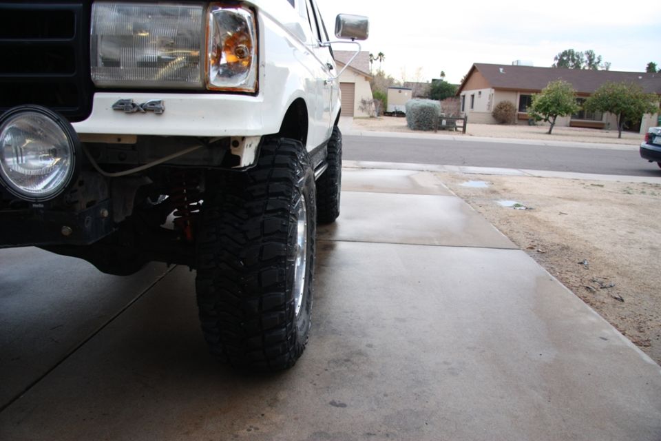 White lifted Ford Bronco front corner with mud tire and 4x4 badge on driveway