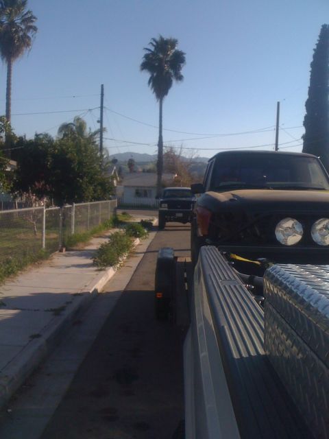 1992 Ford Ranger - A dark-colored truck is being towed by another truck, viewed from the side and slightly from the front.