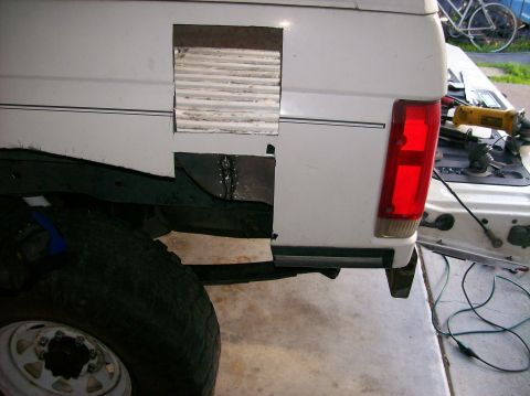 1989 Ford Bronco - The rear quarter panel of a white SUV shows a cut-out section and a red taillight, with tools visible in the background.