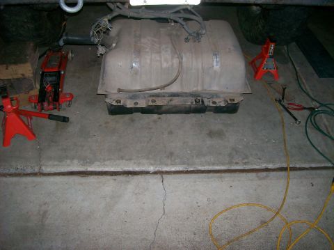 1989 Ford Bronco - Fuel tank removed from vehicle, supported by jack stands. Tools and wiring are visible.