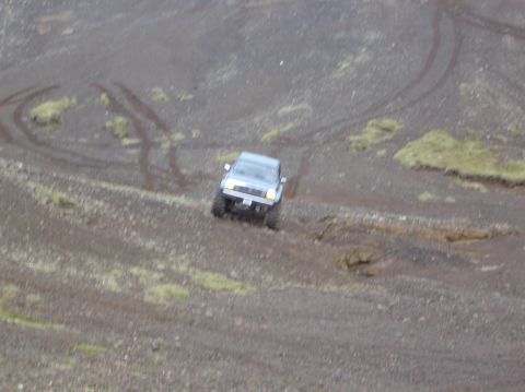 1996 Ford Bronco - A light blue SUV navigates a challenging dirt terrain, leaving tire tracks behind.