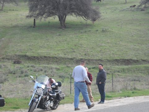 1991 Ford Bronco - A motorcycle is parked on the side of a road with several people gathered around.