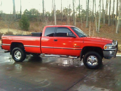 1989 Ford Bronco - This red Dodge Ram pickup truck is shown from the side, parked on a wet surface.