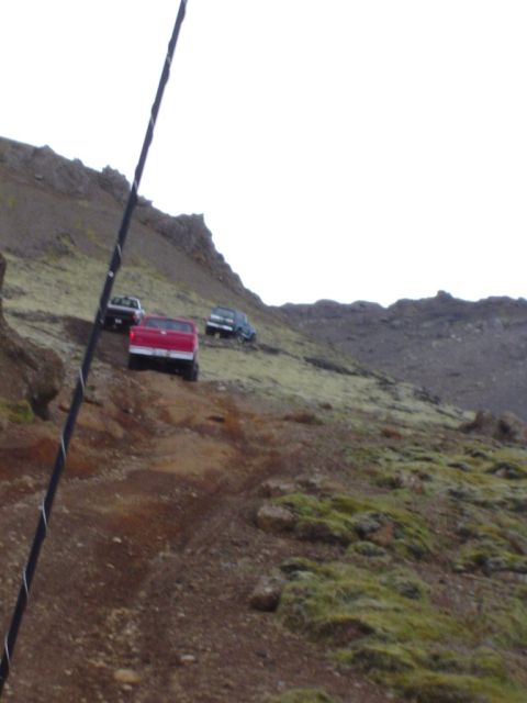 1996 Ford Bronco - Multiple 4x4 vehicles navigate a challenging off-road trail on a barren, mossy slope.