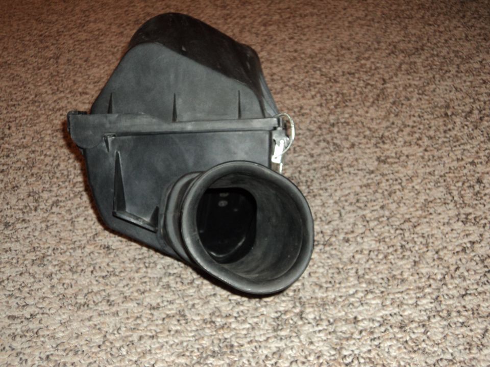 Black plastic air intake box with a wide opening, resting on carpet