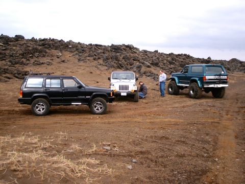 1996 Ford Bronco - Three SUVs are parked on a dirt road with rocky hills in the background under an overcast sky.