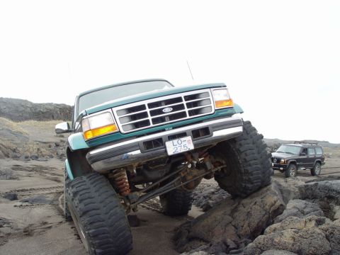 1996 Ford Bronco - A lifted 1996 Ford Bronco navigates rocky terrain, with another SUV visible in the background.