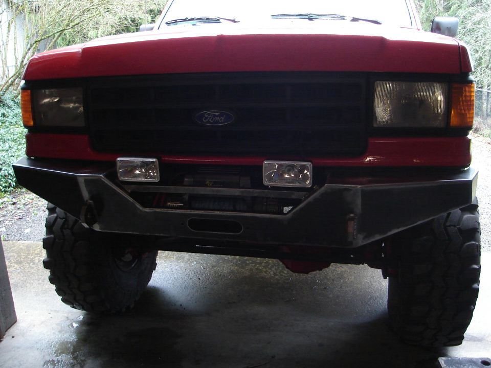 Front view of a red Ford truck with a custom bumper and winch. The grille has a Ford logo
