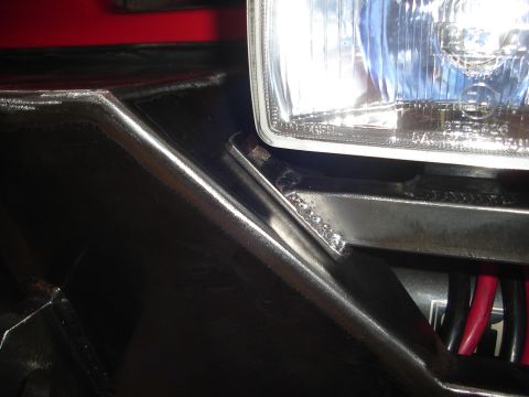 1989 Ford Bronco - Close-up view of a vehicle's front bumper bracket and headlight assembly, showing welded construction and wiring.