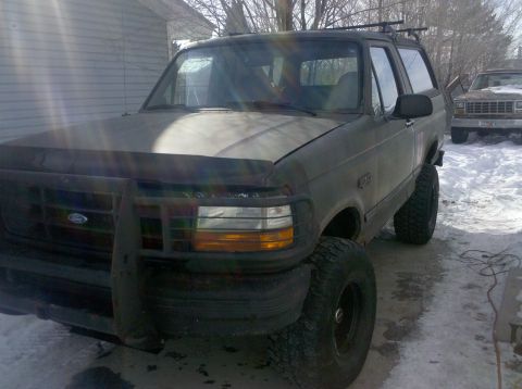 1995 Ford Bronco - A dark green Ford Bronco with a bull bar and large tires is parked in a snowy area next to another vehicle.