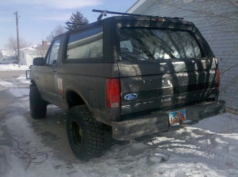 1995 Ford Bronco - Rear view of a 1995 Ford Bronco with a roof rack, parked in a snowy area. License plate is visible.