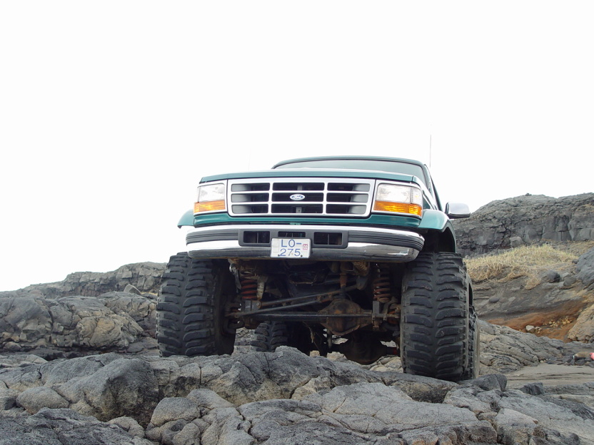 Green and white lifted Ford SUV on big tires climbing rocks, front view