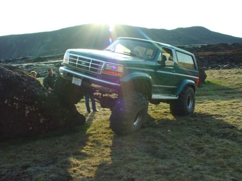 1996 Ford Bronco - A modified green Ford Bronco navigates a rocky obstacle under a bright sun.
