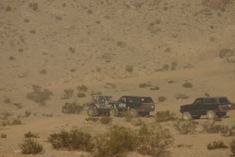1992 Jeep Wrangler - Multiple off-road vehicles navigate a dusty, arid terrain with sparse vegetation and rocky hills in the background.