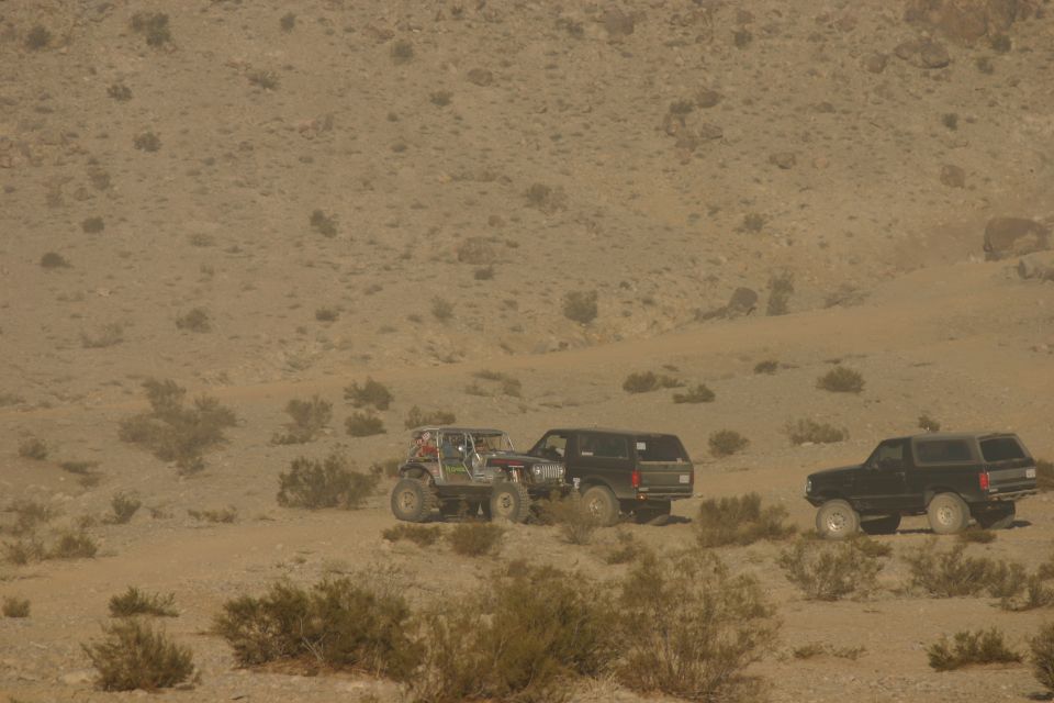 Three off-road vehicles in a dusty desert environment