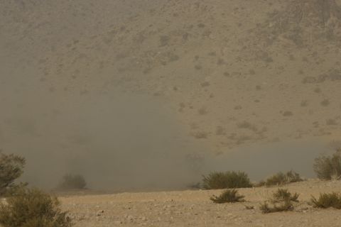 1992 Jeep Wrangler - A large dust cloud hangs over a dry, barren terrain with scattered bushes and hills in the background.