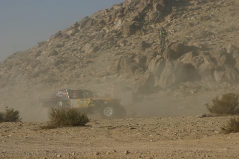 1992 Jeep Wrangler - Off-road buggy competes in a desert race, navigating dusty terrain near rocky hills.