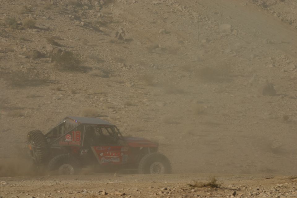 Red off-road buggy with number 18 on the side, kicking up dust on a desert terrain