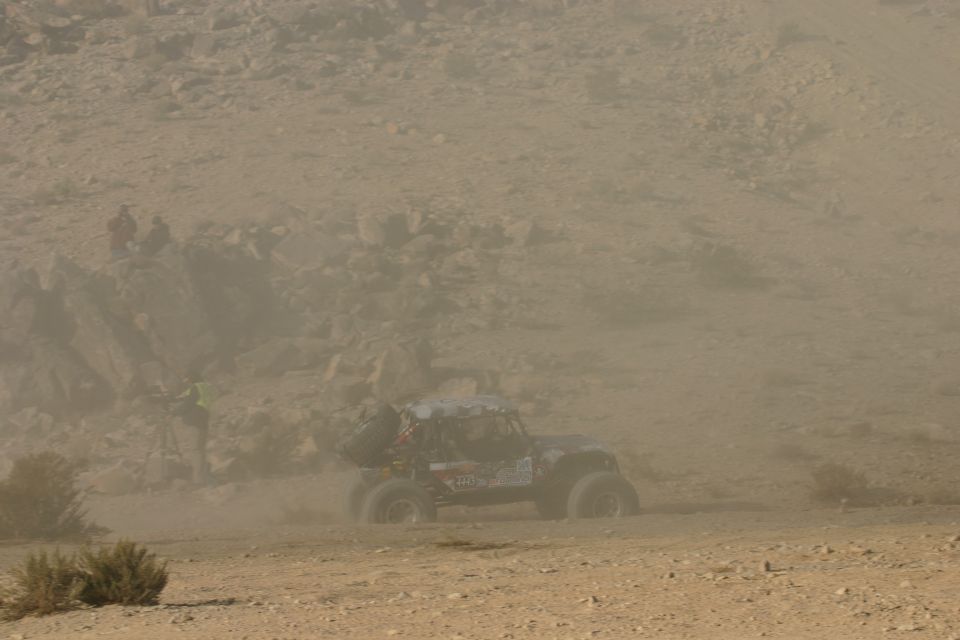 Off-road buggy kicking up dust on a dirt track with spectators on a hill in the background
