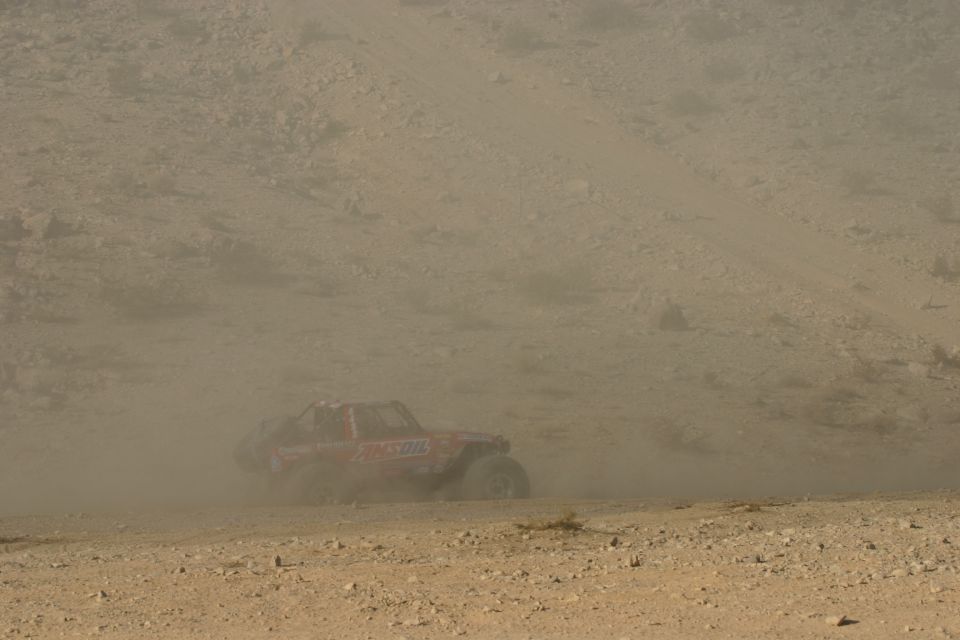 Red off-road racing vehicle kicking up dust on a dirt track