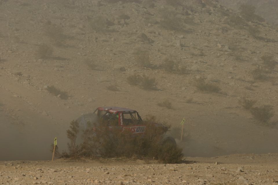 Red off-road vehicle kicking up dust on a desert course
