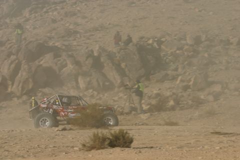 1992 Jeep Wrangler - Off-road buggy competes in a desert race, kicking up dust. Spectators and a cameraman observe the event.