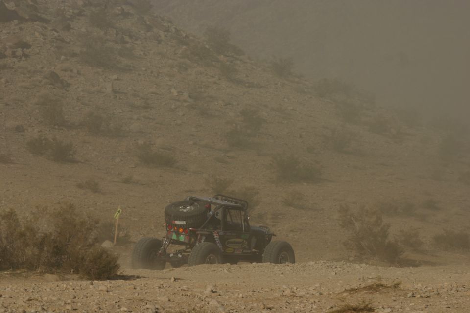 Off-road buggy with large tires and spare tire on back, kicking up dust on a dirt path