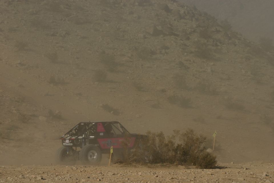 Red off-road buggy with roll cage driving through dust on a desert course