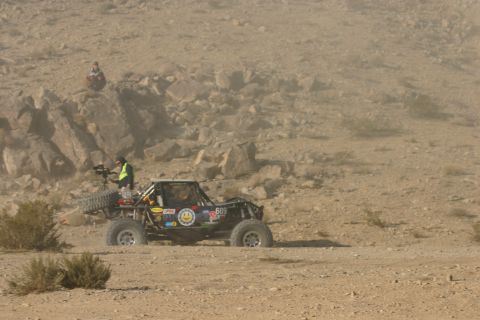 1992 Jeep Wrangler - Off-road buggy competes in a desert race, kicking up dust. A person operates camera equipment nearby.